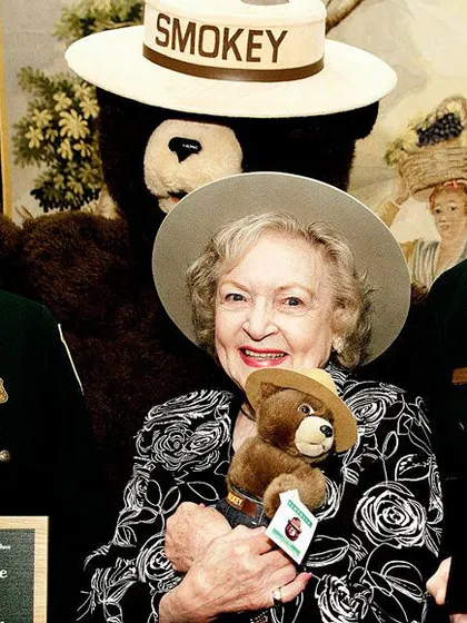 Betty White sosteniendo un peluche del oso Smokey