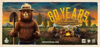 Smokey de pie junto a los campistas sentados cerca de una fogata, el texto dice 80 años de prevenir incendios forestales juntos